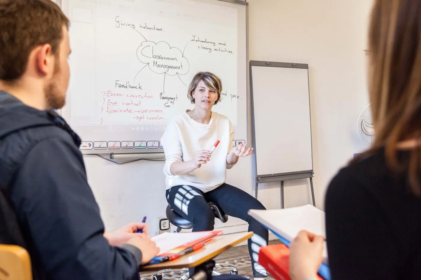 A trainer leading a session on classroom management, with a mind map on the whiteboard behind her and trainees taking notes