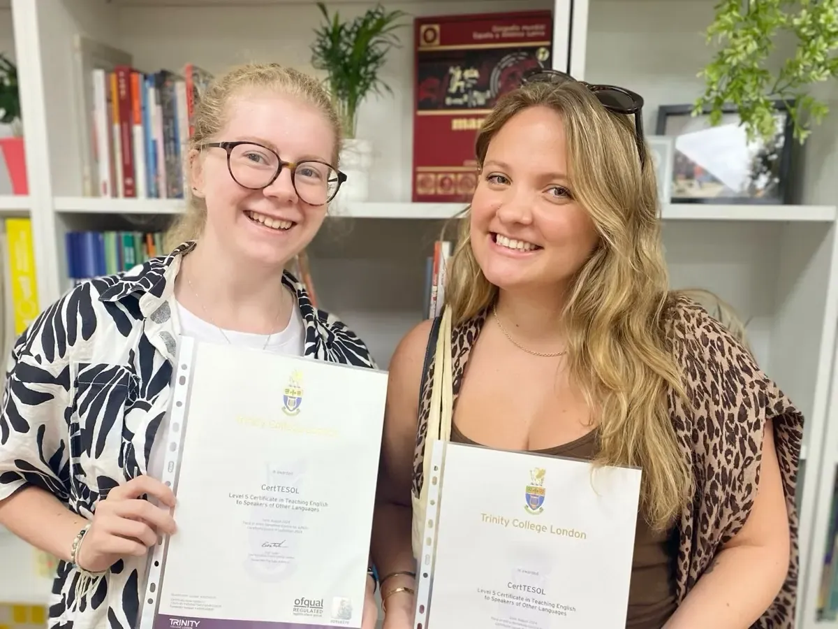 Two smiling TEFL Iberia graduates holding up their Trinity College London CertTESOL certificates