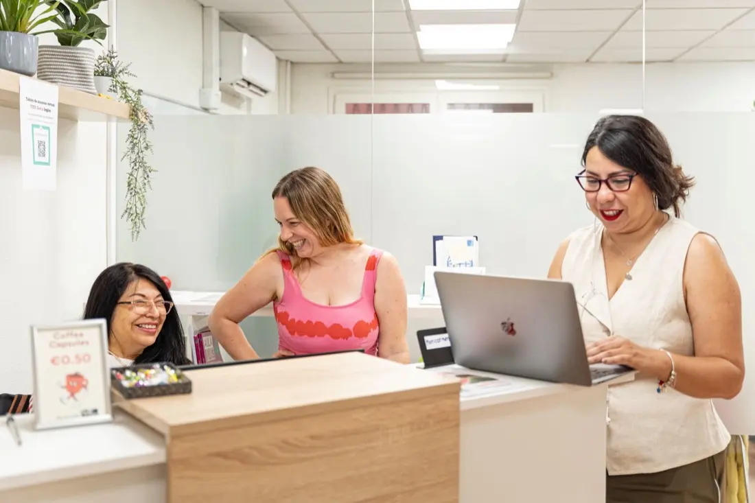 Three members of the TEFL Iberia team chatting and laughing at the reception desk of the school