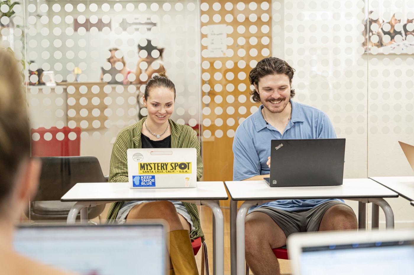 Two trainees smiling at their laptops in a classroom at TEFL Iberia